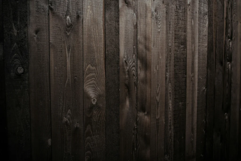 Close-up view of a dark wooden fence with vertical planks showing natural grain and texture.