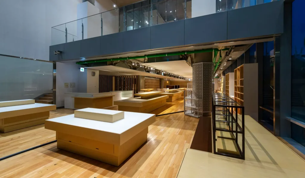 Interior of a modern, empty store with wooden display tables, shelves, and a glass upper floor.