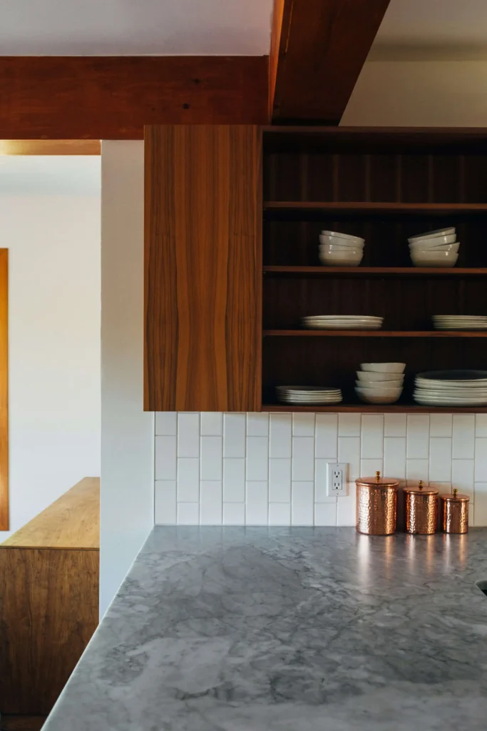 Kitchen with wooden cabinets, open shelves holding white dishes, a marble countertop, and three copper canisters.