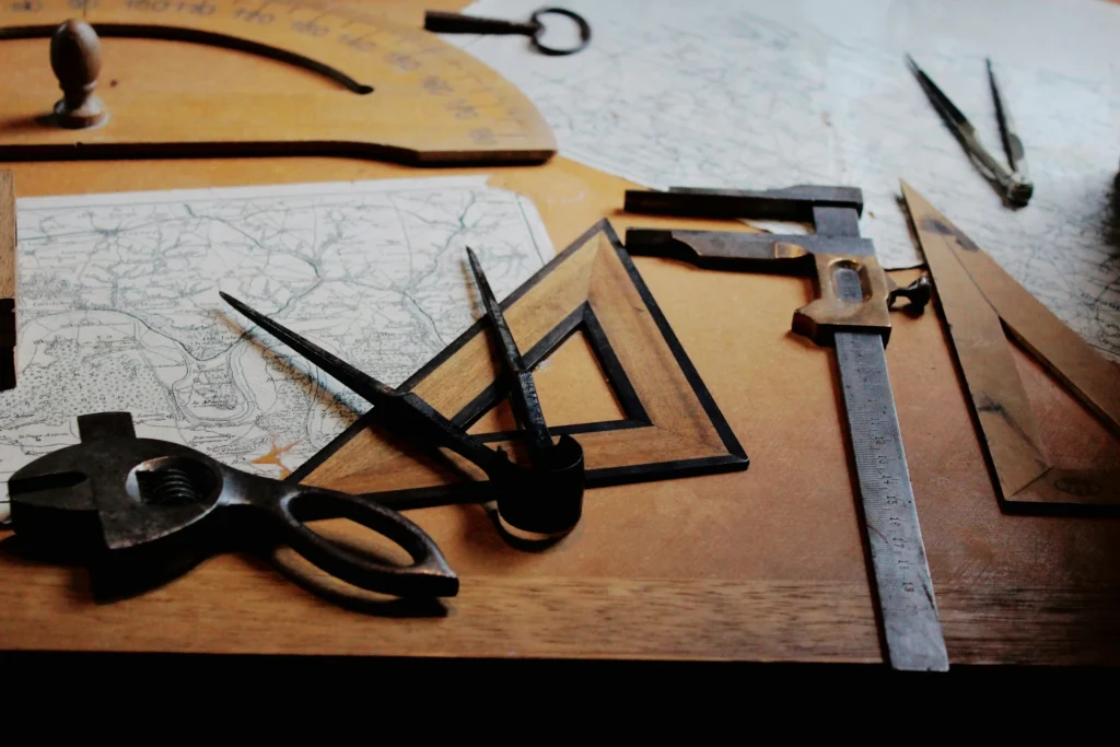 Drawing tools, including compasses, protractors, set squares, and calipers, are placed on a wooden table beside a map.