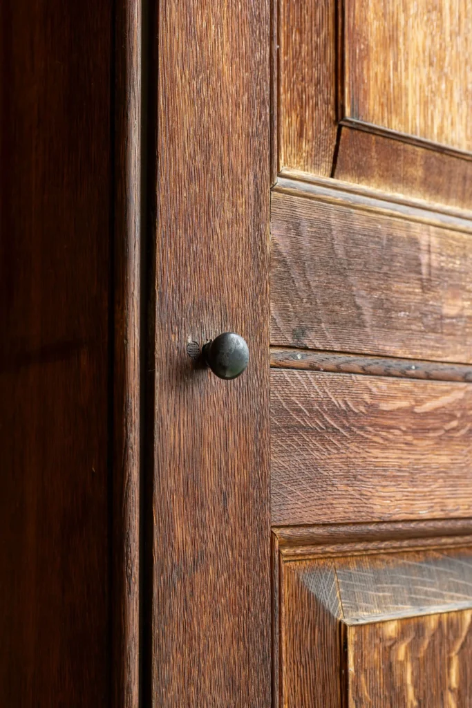Close-up of an old wooden door with a dark metal knob and visible wood grain texture.