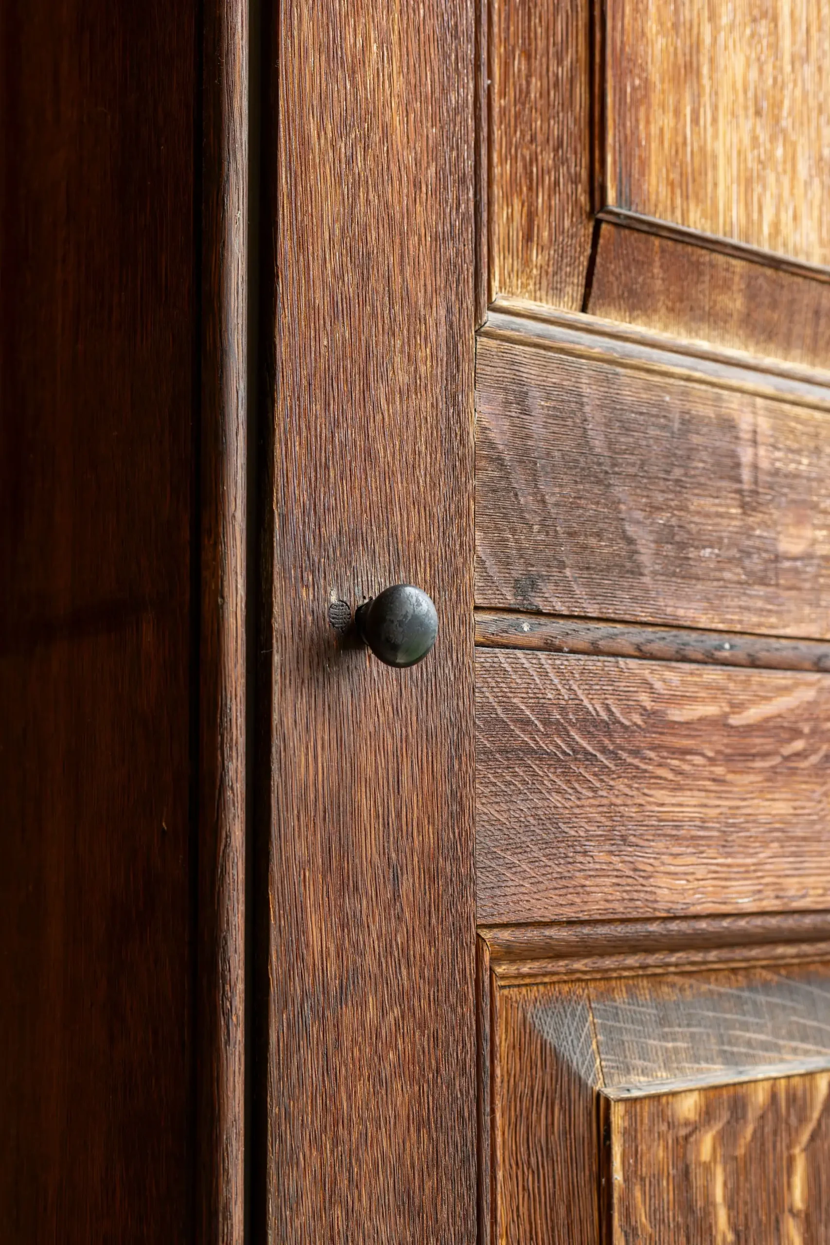 Close-up of an old wooden door with a dark metal knob and visible wood grain texture.