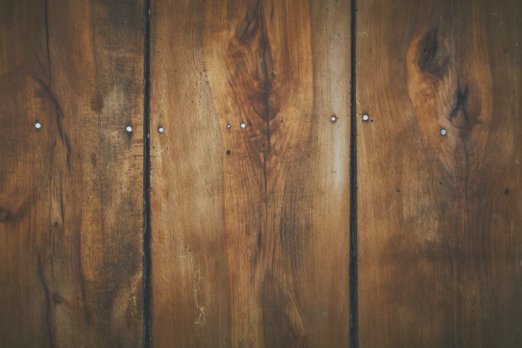 Close-up of wooden planks with visible grain and knots, joined together by small metal nails.