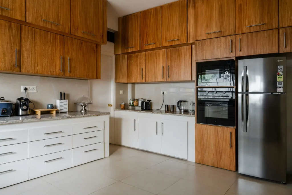 Modern kitchen with wooden cabinets, white drawers, a stainless steel refrigerator, and various appliances on the countertop.
