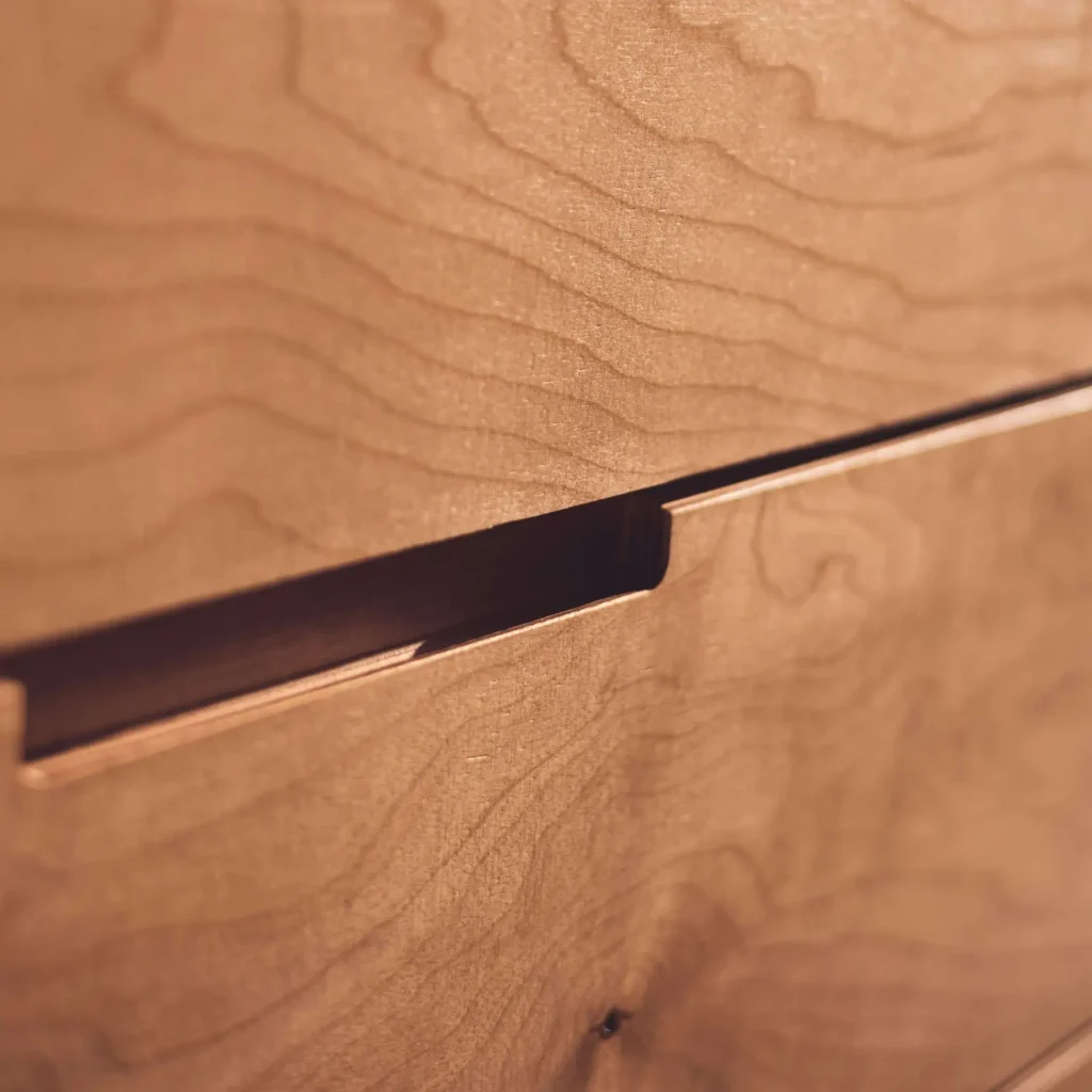 Close-up of wooden drawer with a horizontal groove handle, showing the texture and grain of the wood.